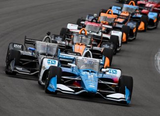 Seven IndyCar cars lining up one behind the other around a corner of a circuit