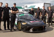 A group of students from the National Motorsport Academy on either side of a black Lotus in the paddock
